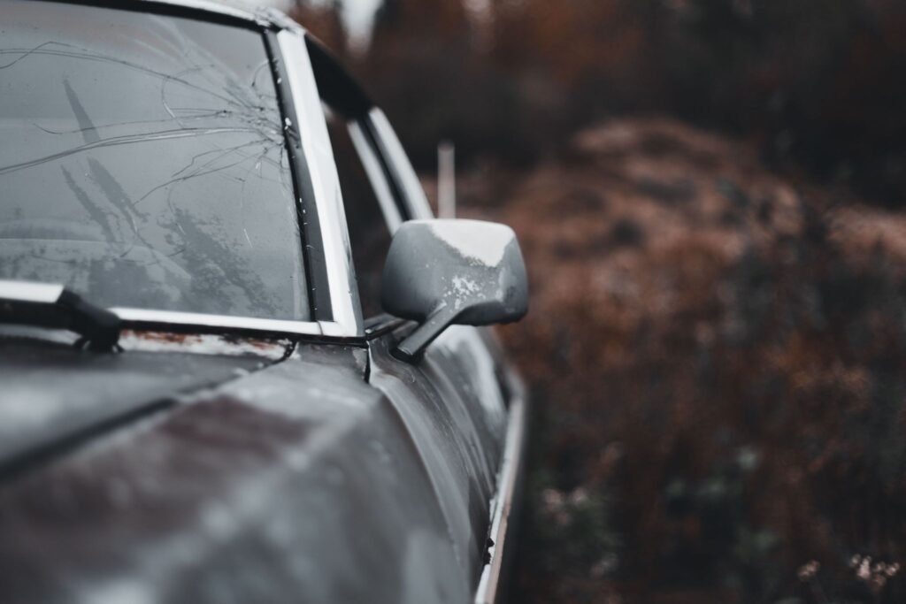 Close-up of a weathered, rusted car with a broken windshield and side mirror in an outdoor setting